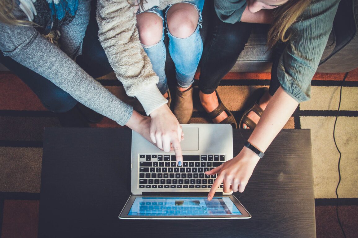 ID: Individuals huddled together, pointing at a laptop screen placed centre frame.